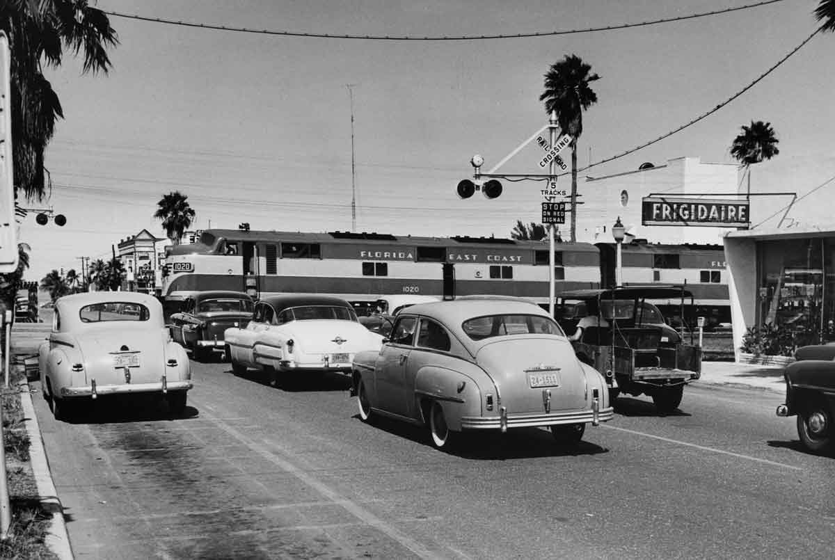 a passenger train crossing a road with cars waiting for it to pas