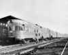 a passenger train and an observation car at a station with people loading supplies onto it