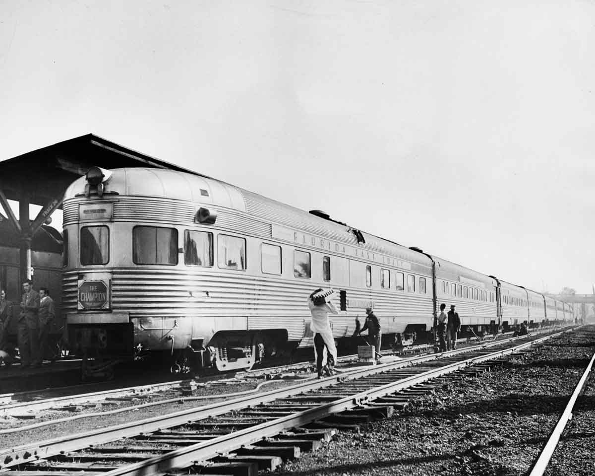 a passenger train and an observation car at a station with people loading supplies onto it