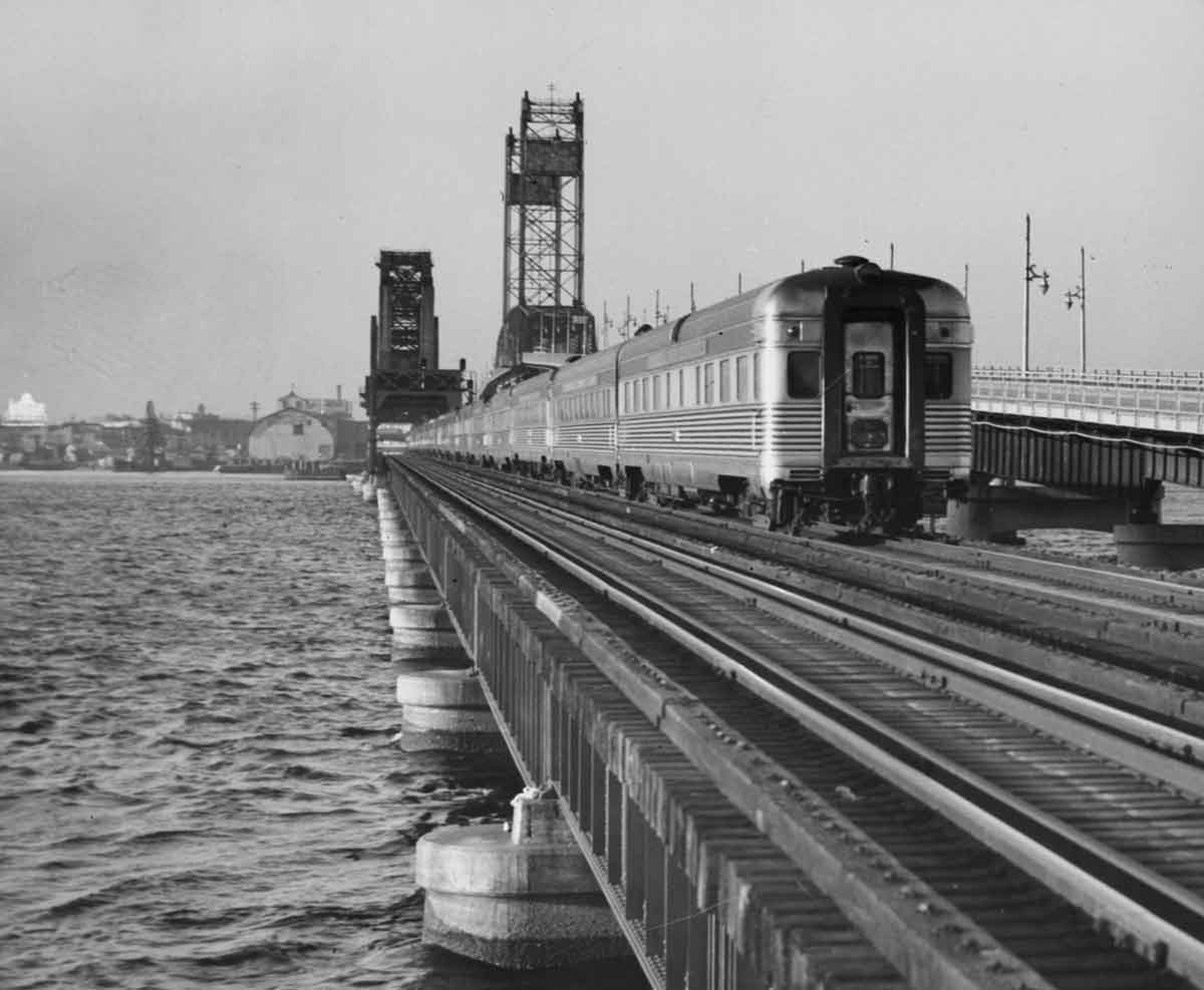 a passenger train crossing a large bridge with Jacksonville in the background