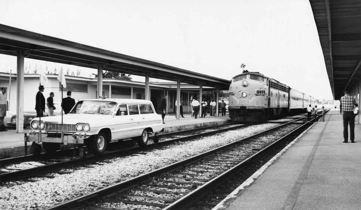 at a passenger station, an automobile is on a set of rails and blocking a passenger train behind it