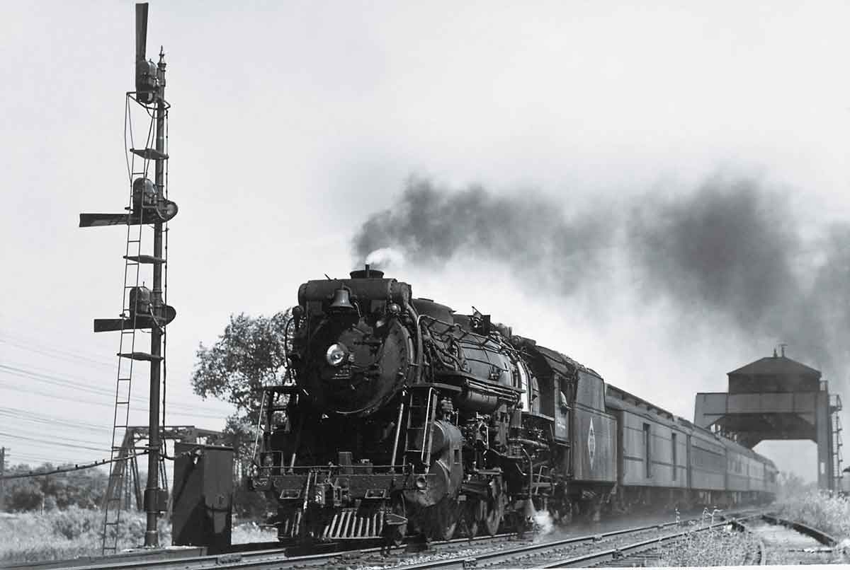 A black and white photo of a train exiting a tunnel