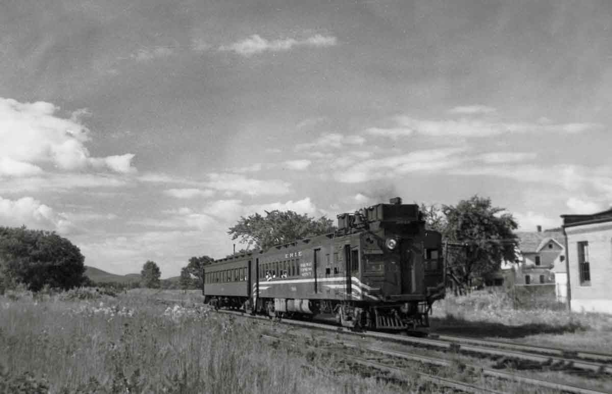 A black and white photo of a train passing through a rural town