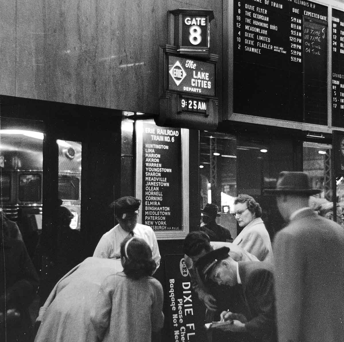 A black and white photo of passengers waiting to give their ticket to get on the train