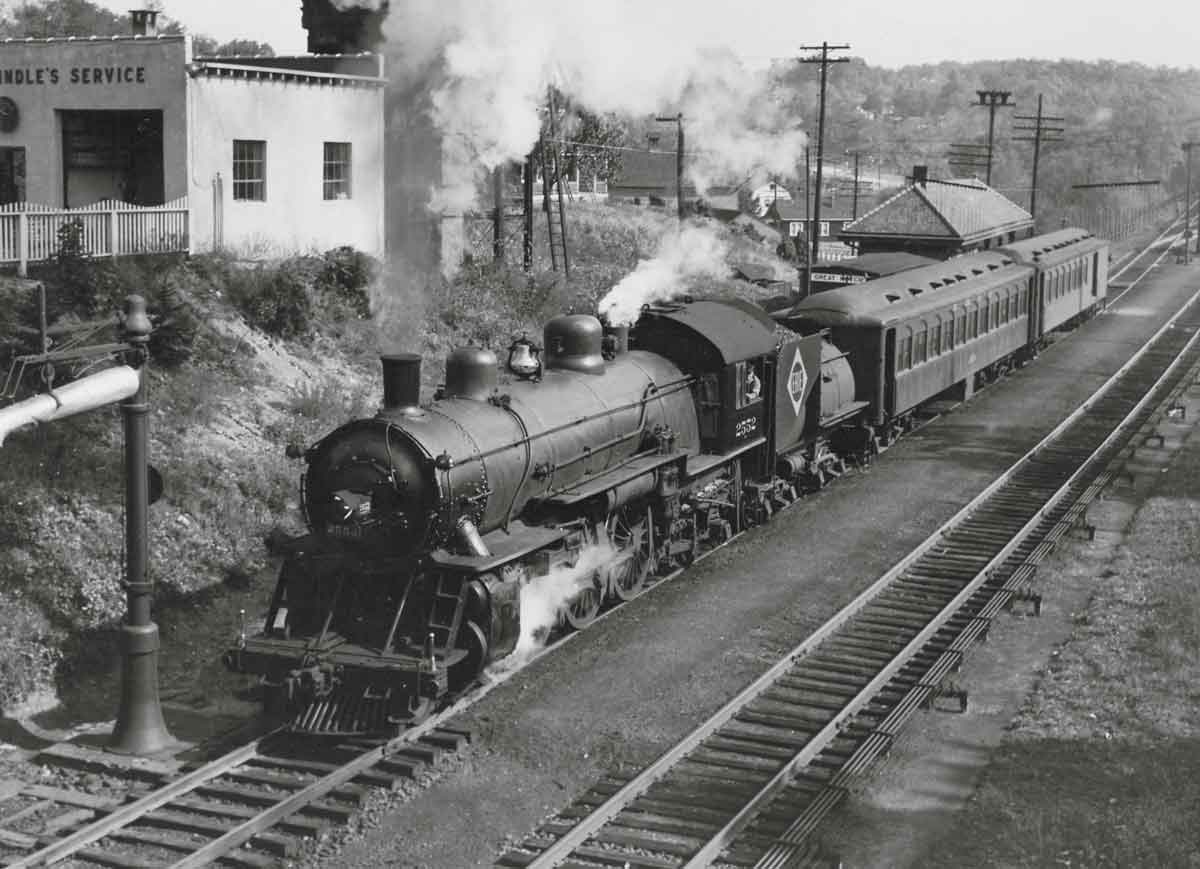 A black and white photo of a train approaching a station