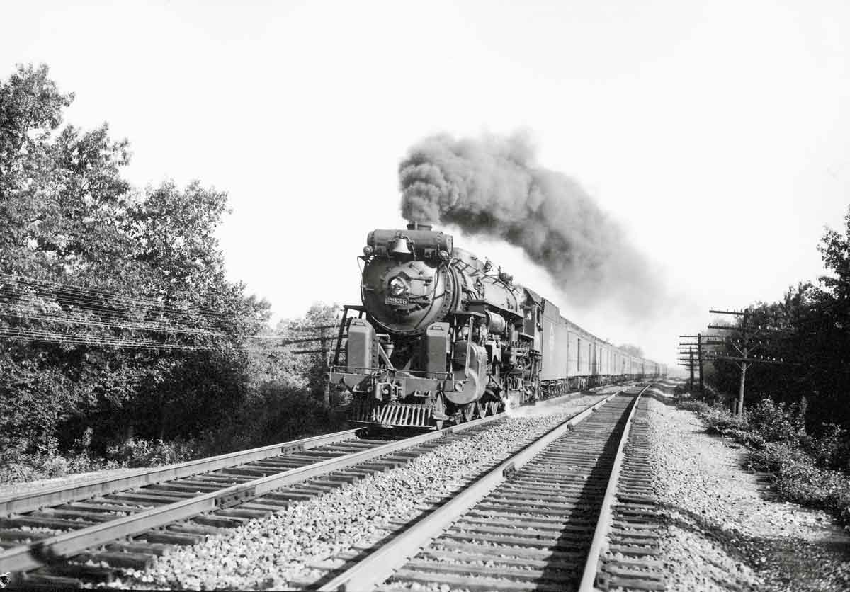 A black and white photo of a train coming down the tracks with smoke coming out of its chimney