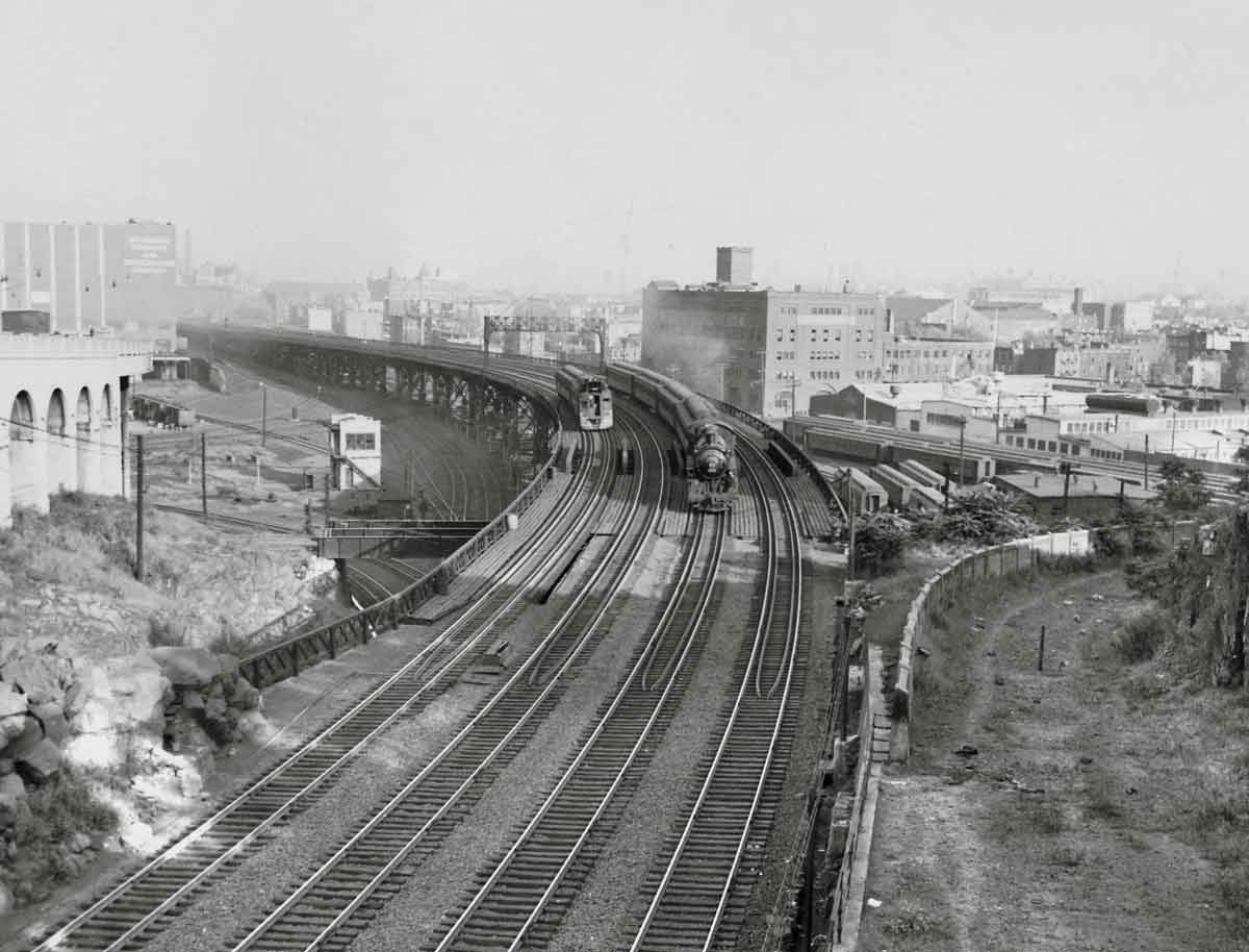 A black and white distant photo of two trains turning a corner at the same time