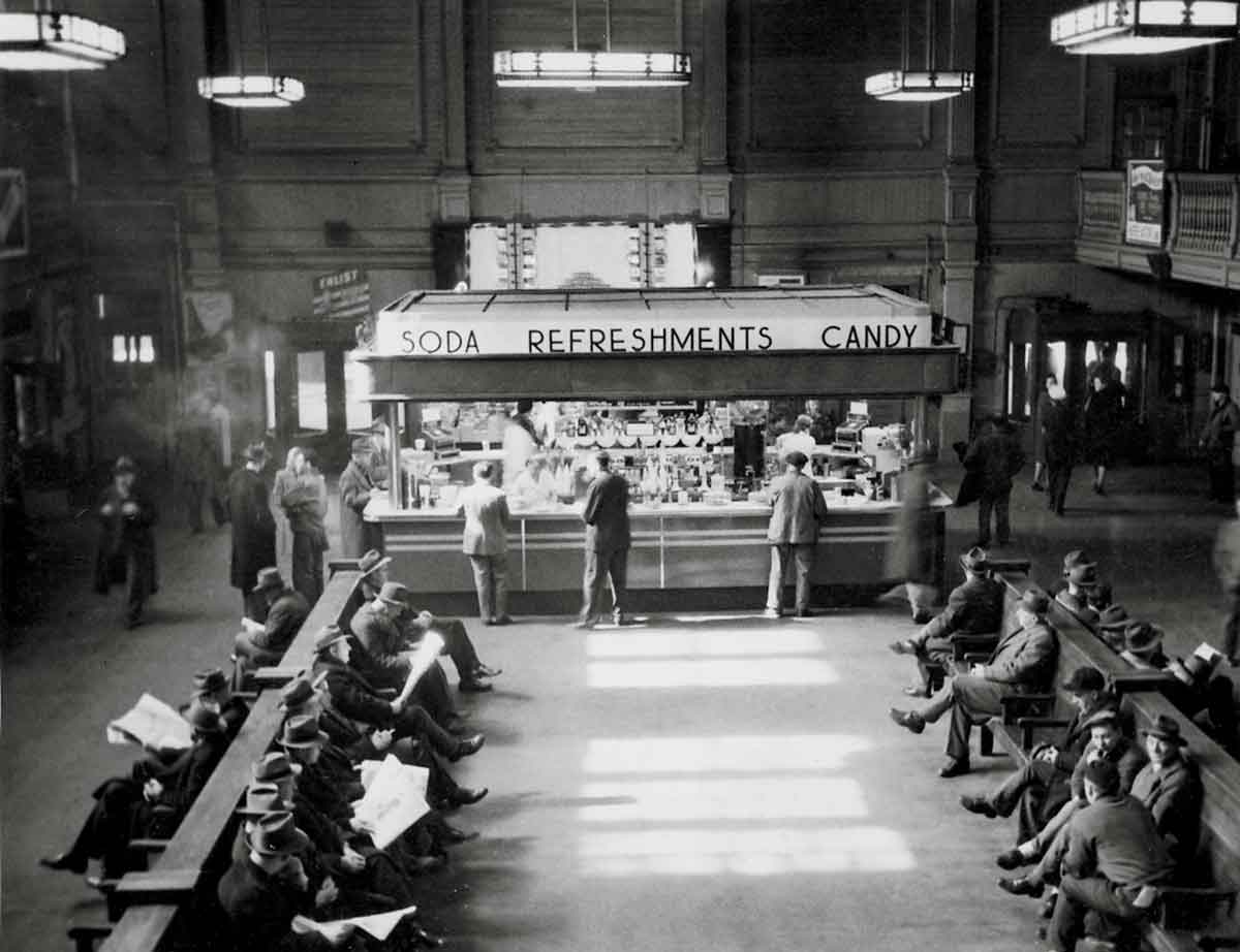 A black and white photo of people purchasing food and sitting at a terminal
