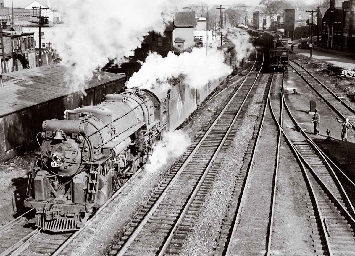 A black and white photo of two trains approaching a station