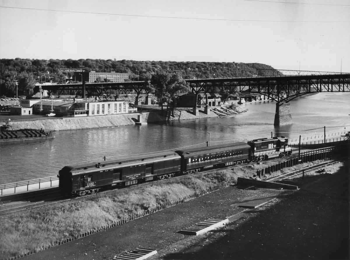 a diesel engine on a rail by a river with St. Paul in the background