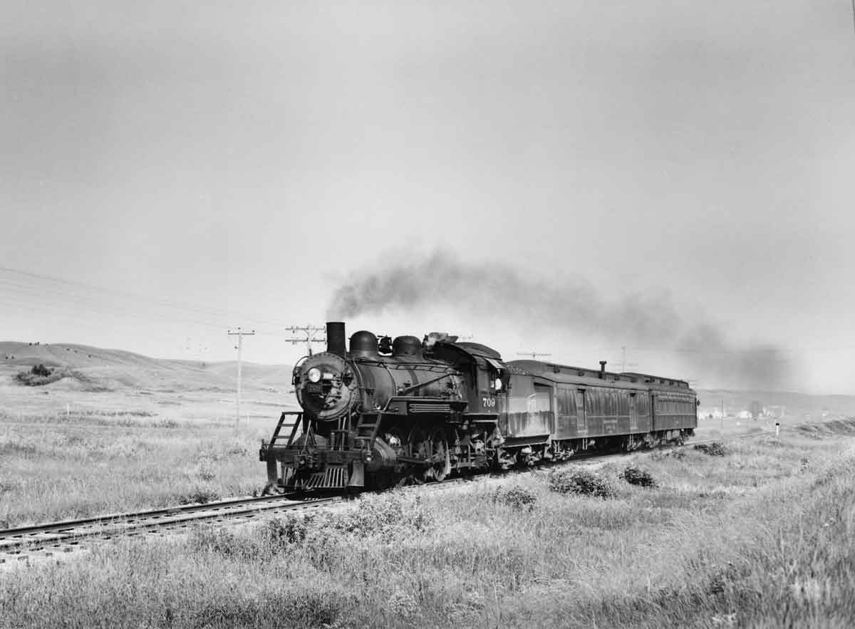 a steam engine passenger train rolling past a field