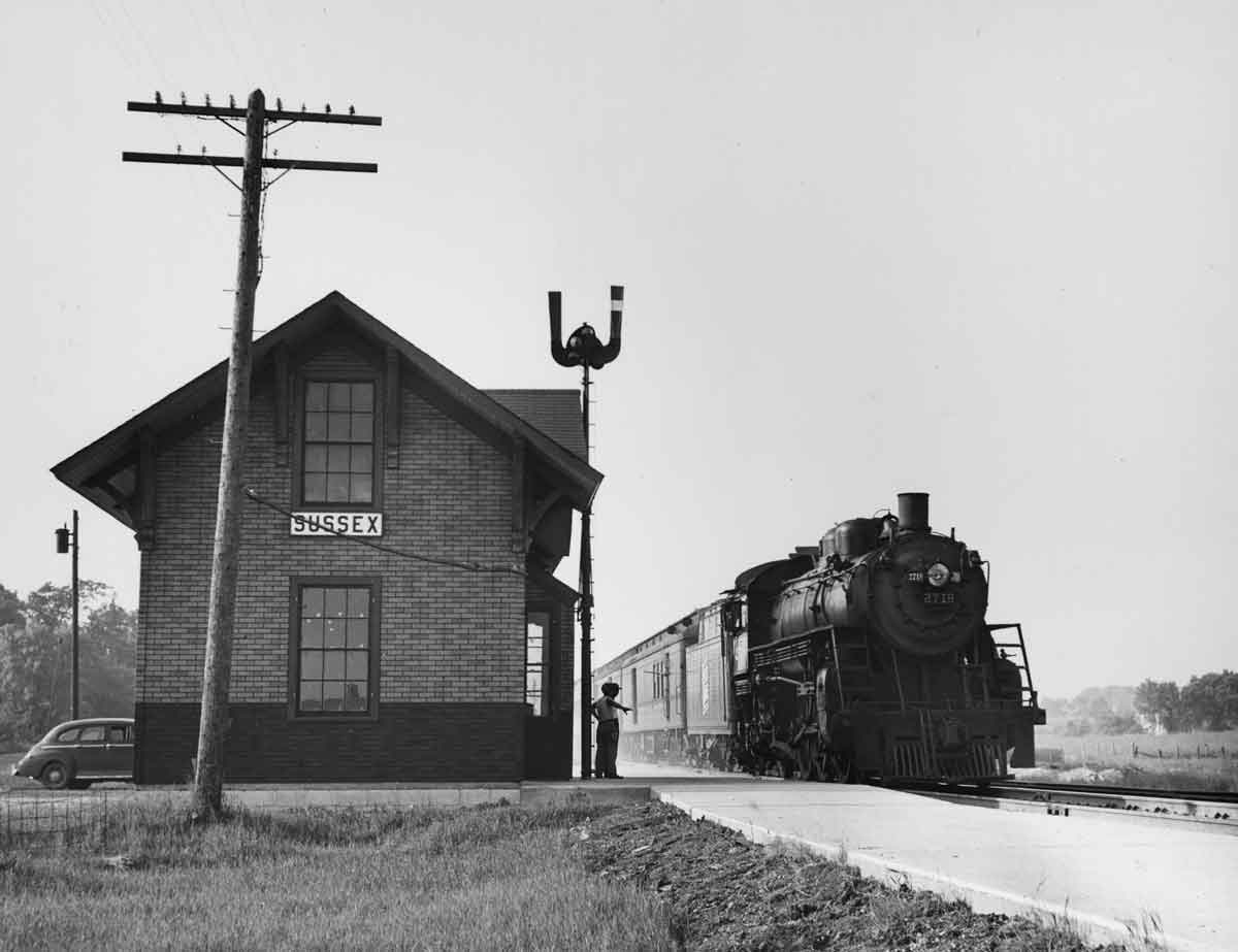 a steam engine passing a flagstop with it's mail hook extended