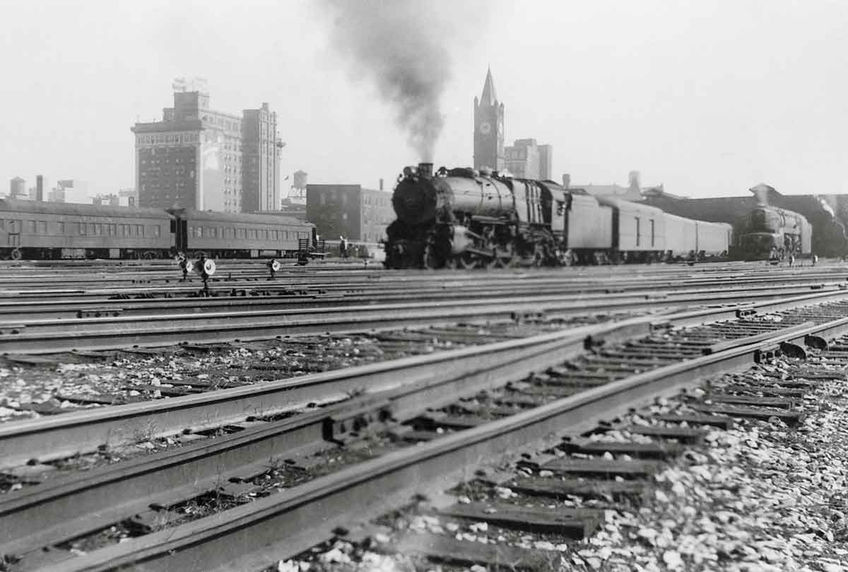 A distant shot of a train pulling into a train station with buildings in the background