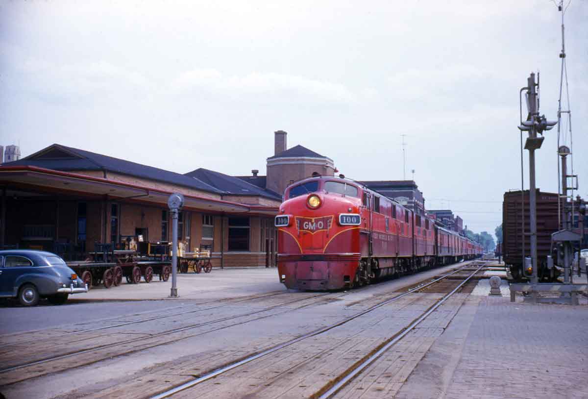 a diesel and passenger cars by a train station