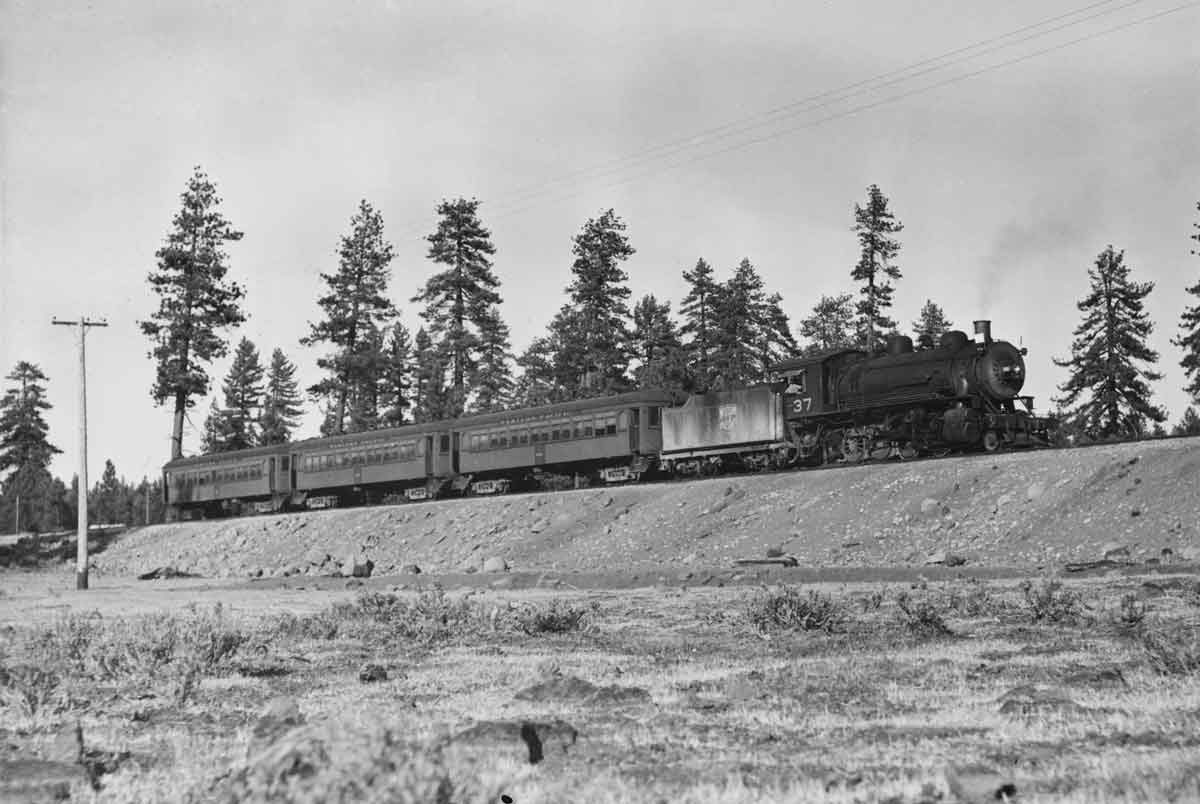 a steam engine with passenger cars rolling past a patch of trees