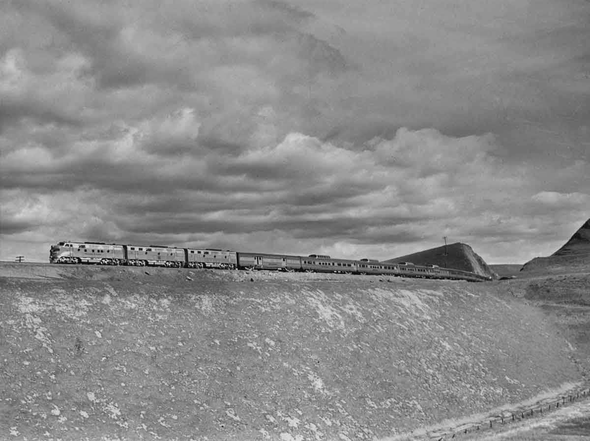 a diesel pulling passenger cars on a hill under a cloudy sky
