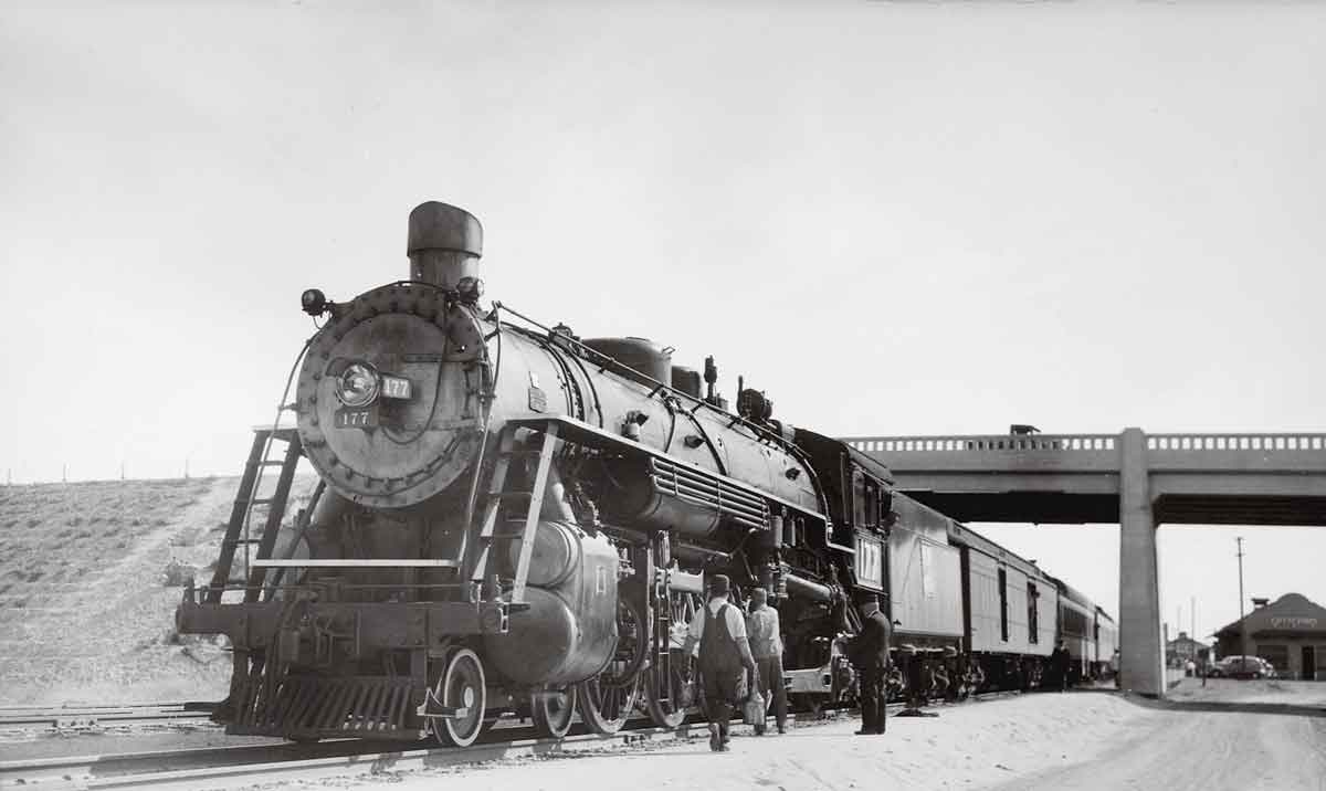 a steam engine and passenger cars under a bridge