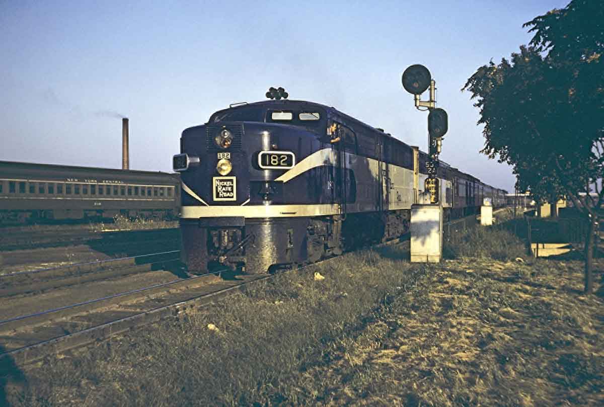 A blue and yellow train sitting in a grassy area next to a stop light
