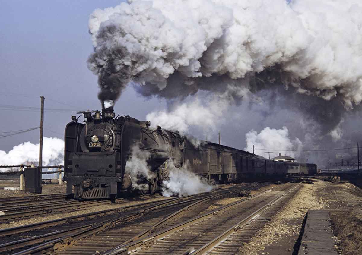 A train passing by with big white smoke coming out of its chimney