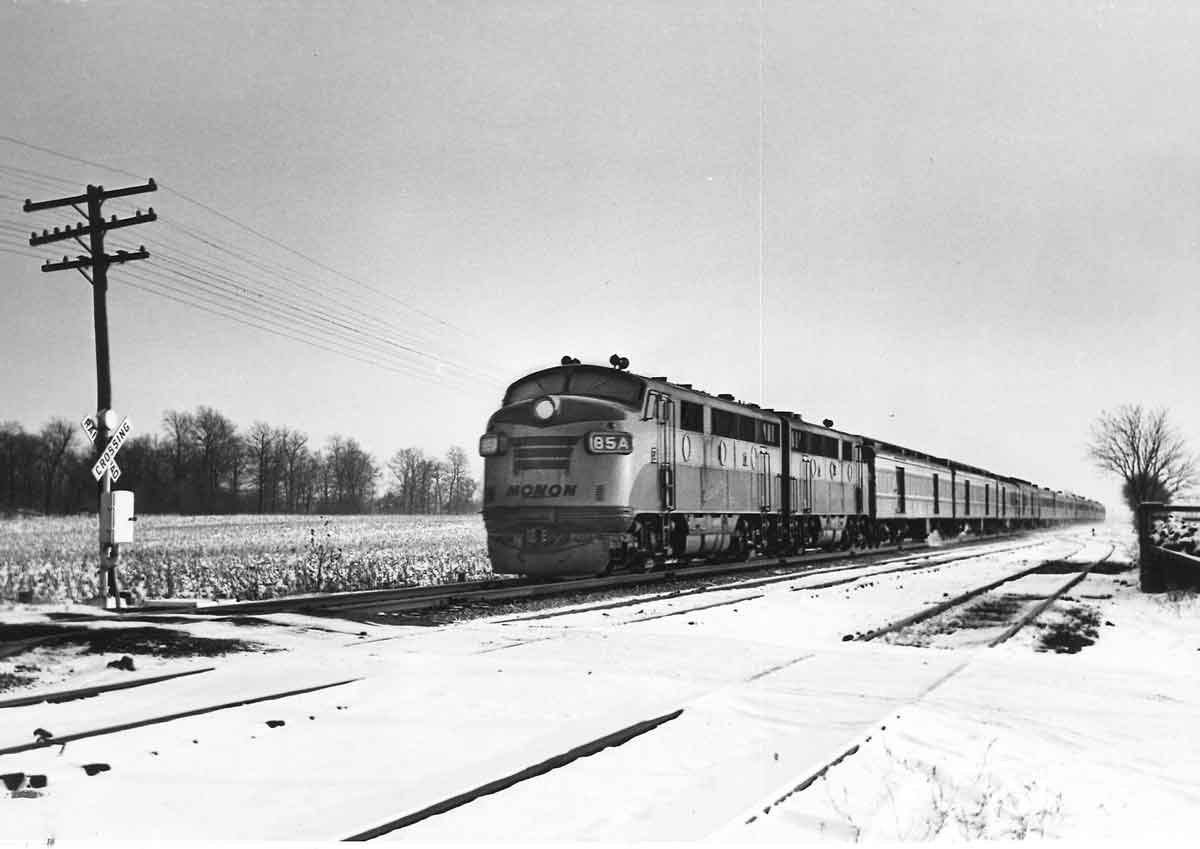 a diesel pulling passenger cars past a snowy field
