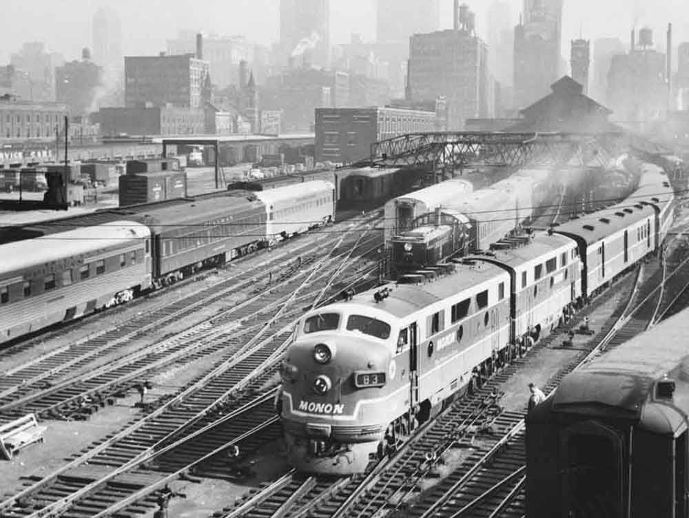 three passenger trains by a train station, with a the train in the foreground leaving the area