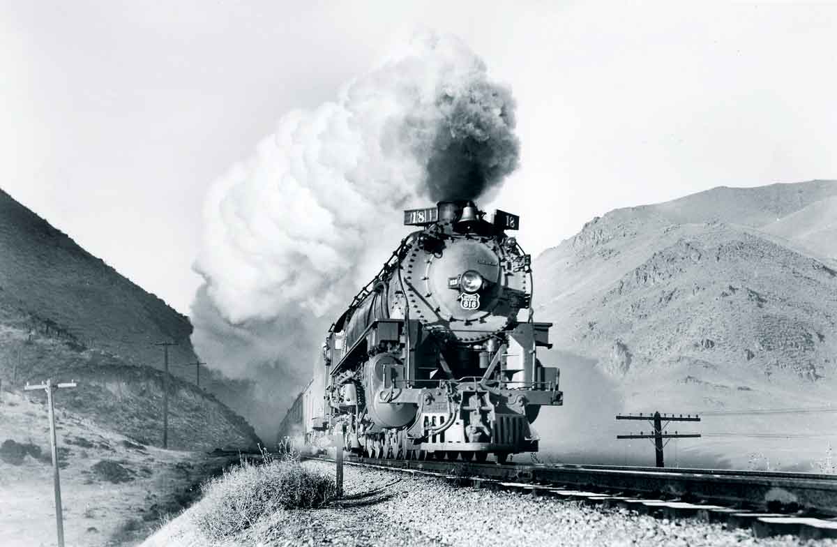 Smoking steam locomotive with passenger train between mountains