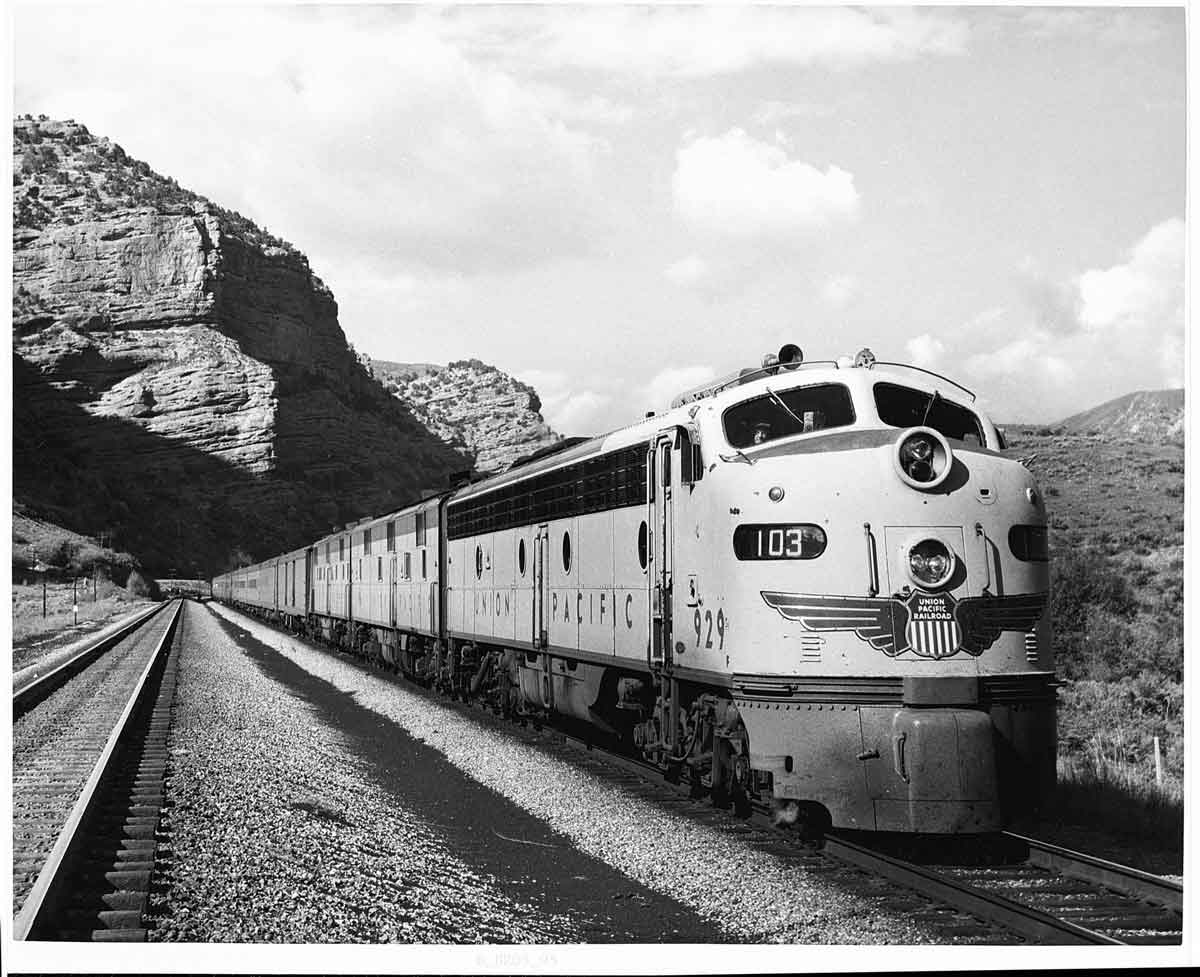 Streamlined diesel locomotives lead passenger train away from mountain cliffs
