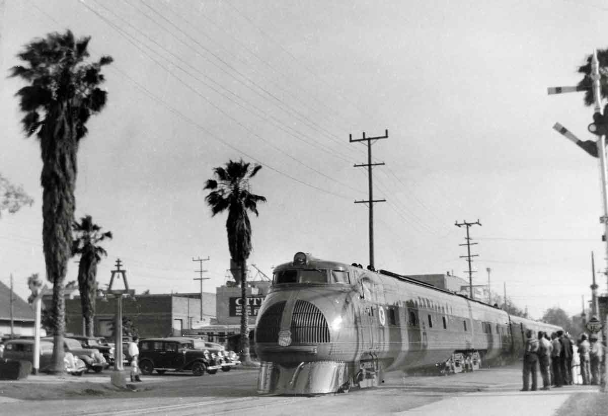 Passengers watch early streamlined passenger train by palm trees