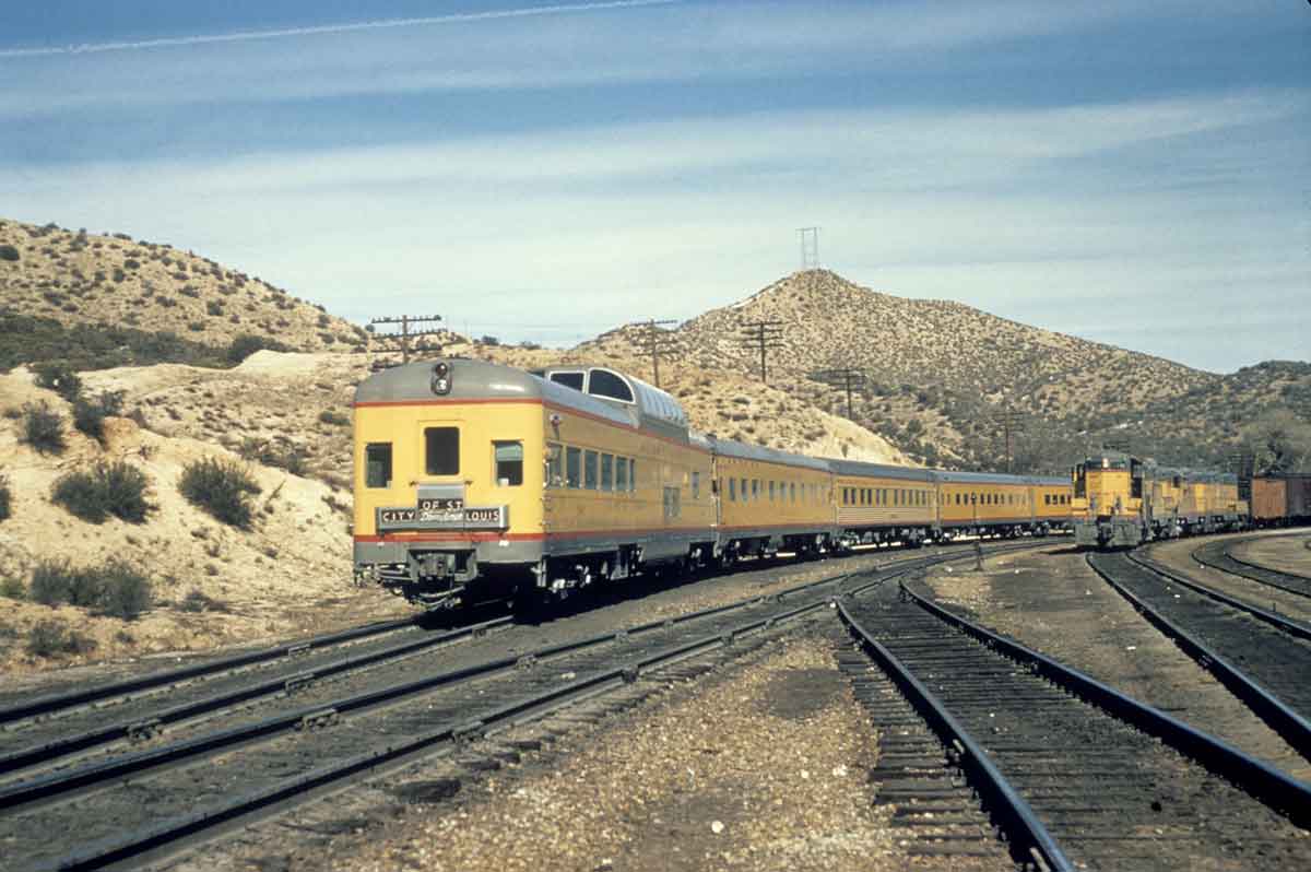 Rear of yellow passenger train passing diesel freight locomotive