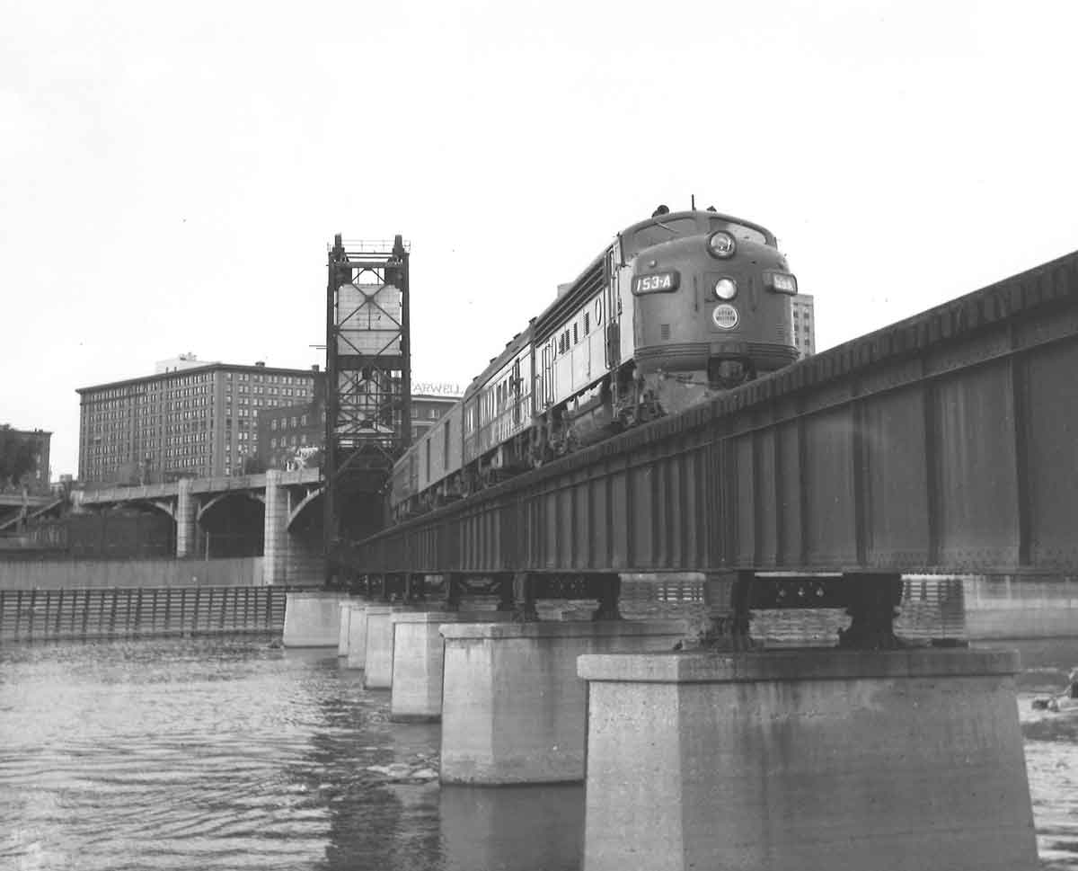 A black and white photo of a train travelling over a bridge