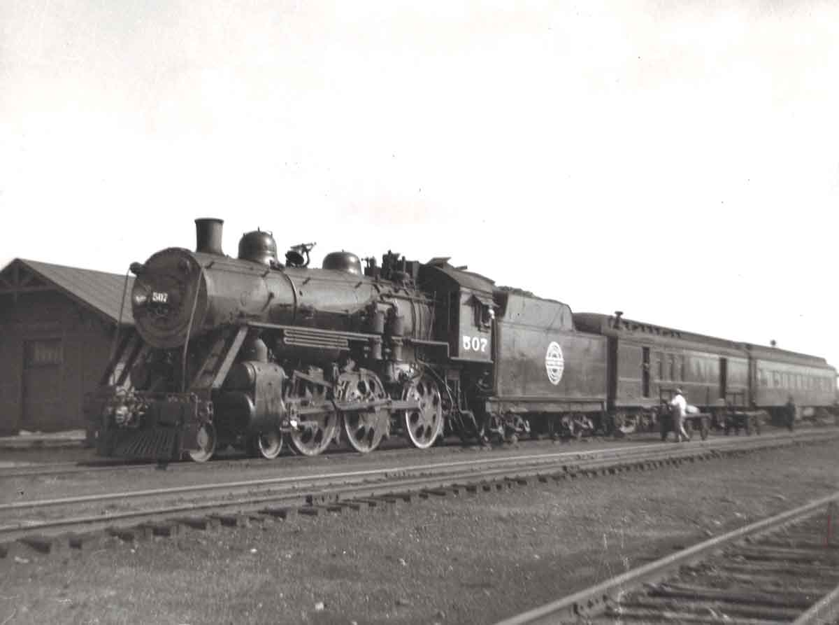 A black and white photo of a man approaching a train