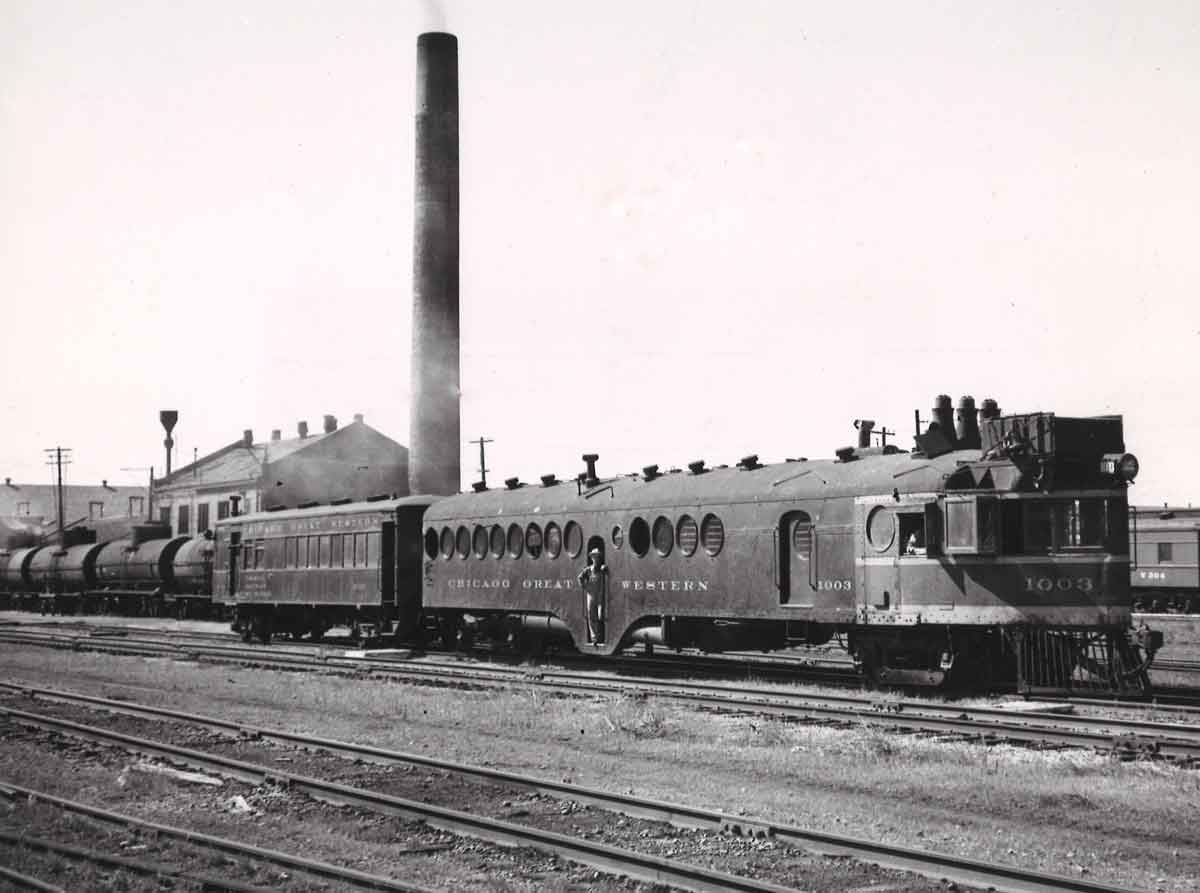 A black and white picture of a train parked outside a station