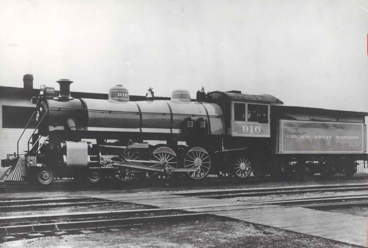 A black and white photo of a train parked outside a station