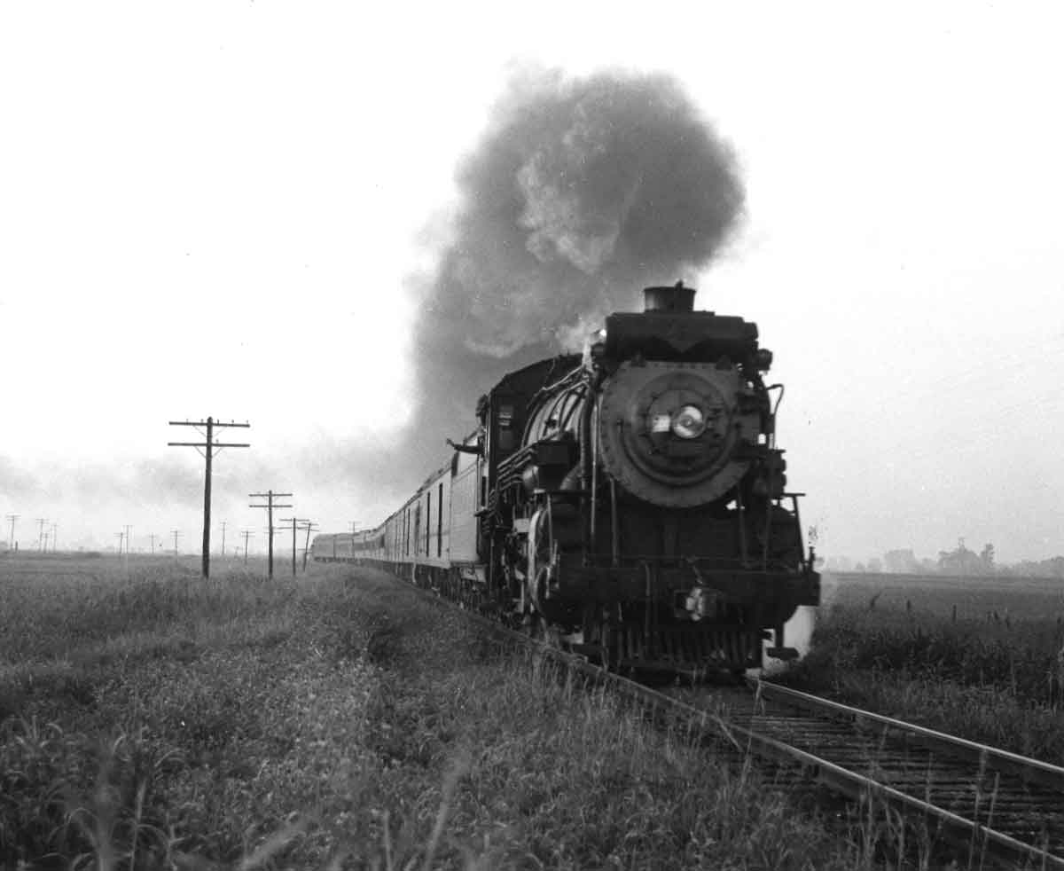 A black and white picture of locomotive 4-6-2 702 on the tracks with smoke coming out
