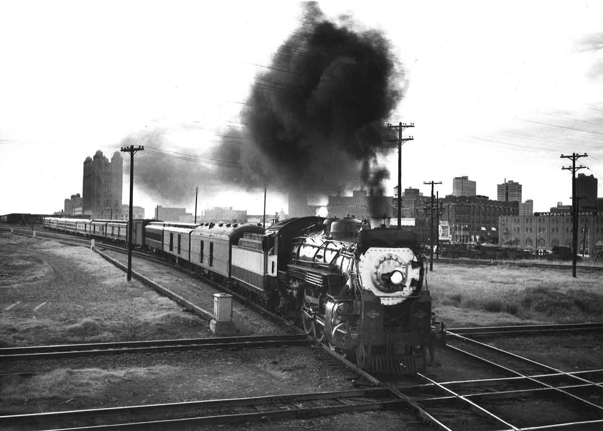 A black and white photo of locomotive 4-6-2 702 crossing a railroad intersection