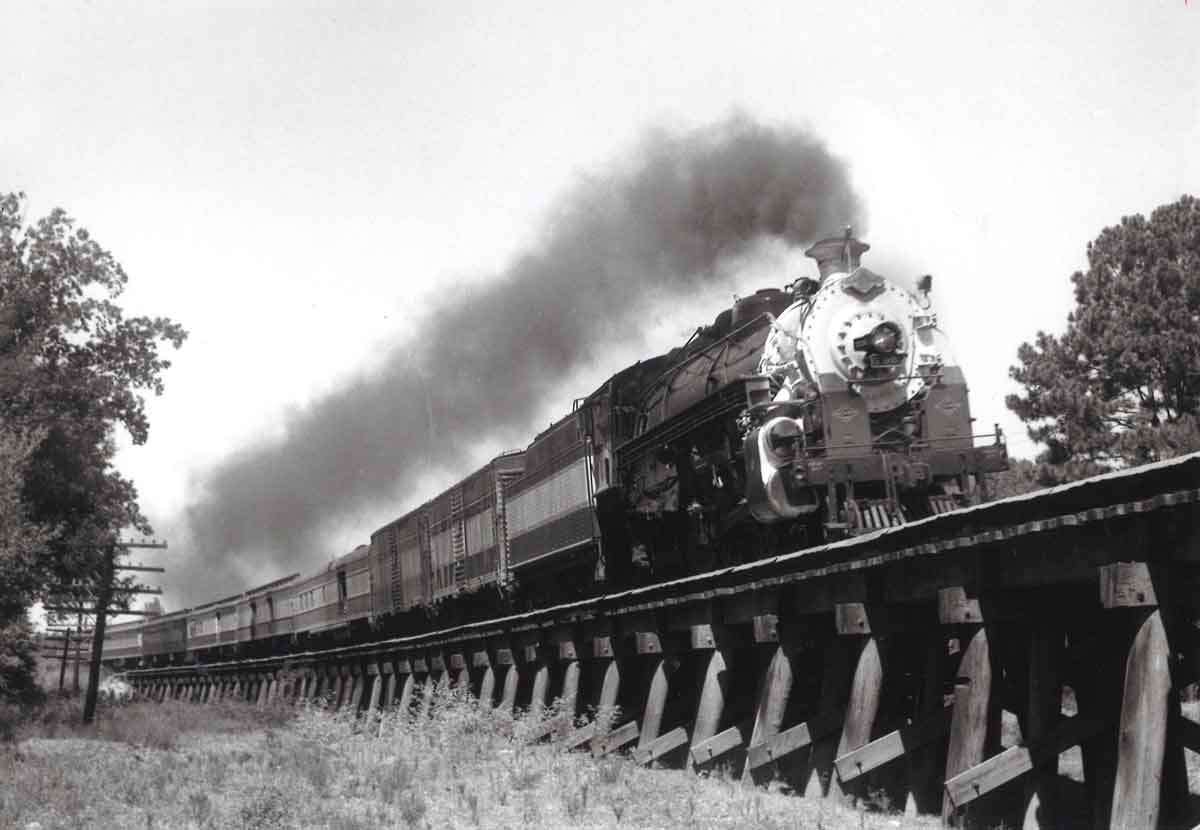 A black and white picture of locomotive 4-6-2 706 traveling down a raised railroad track with steam coming out of the chimney