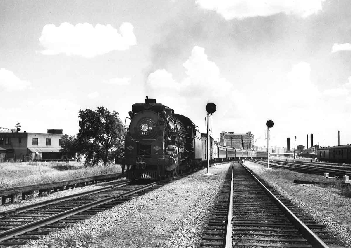 A black and white photo of locomotive 4-6-2 715 passing a stop light