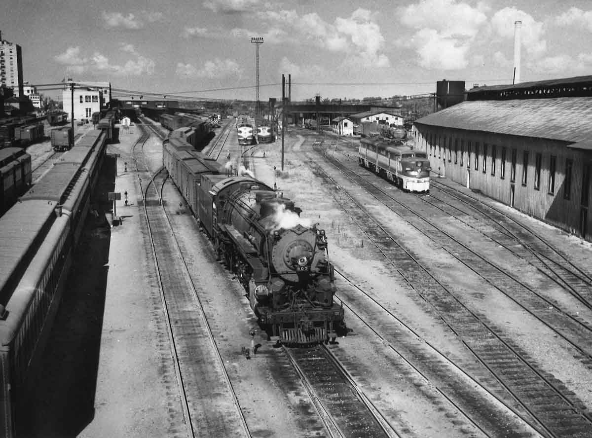 A black and white photo of locomotive 4-8-2 907 leaving the rail yard