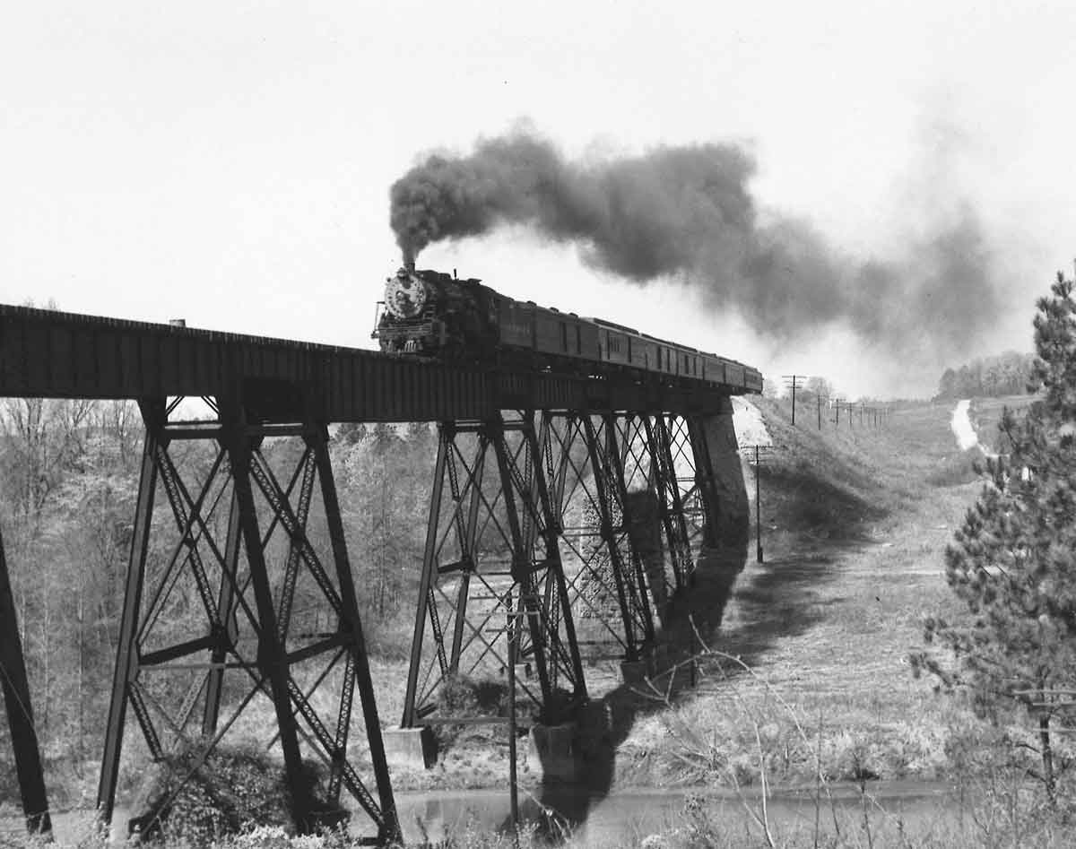 a stream engine passenger train on a tall bridge over a river