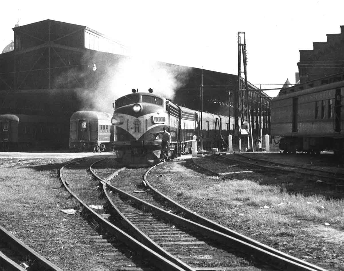 A diesel passenger train with a station in the background