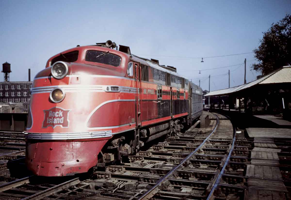 A red and orange train parked outside a station