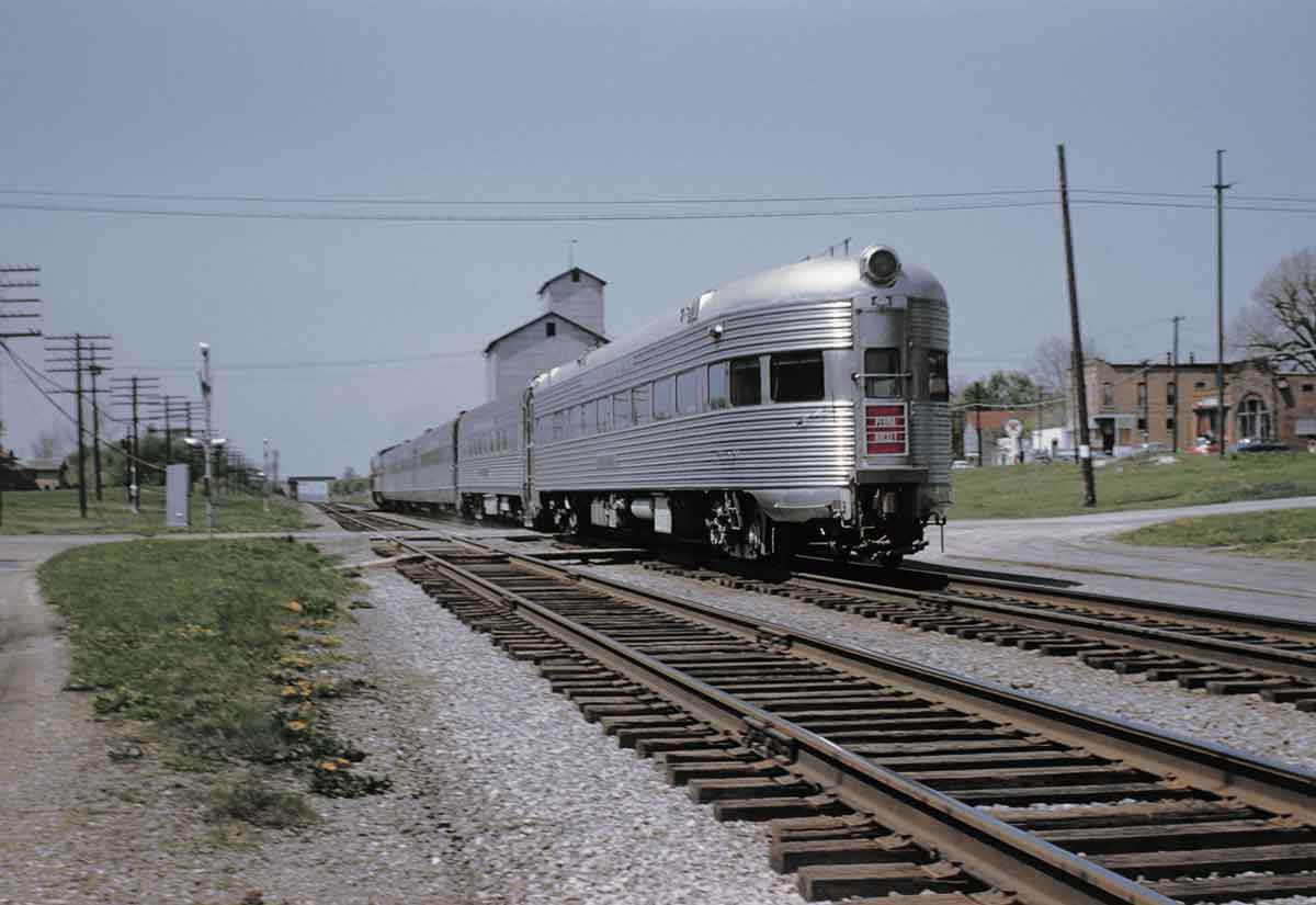 A silver train passing through a small town