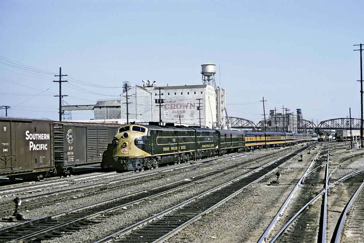 A yellow diesel locomotive pulling cars through a train yard