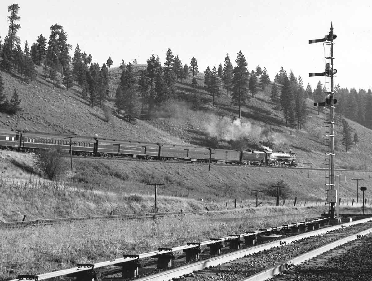 a black and white photo of a train with a steam engine in front of a hill and trees
