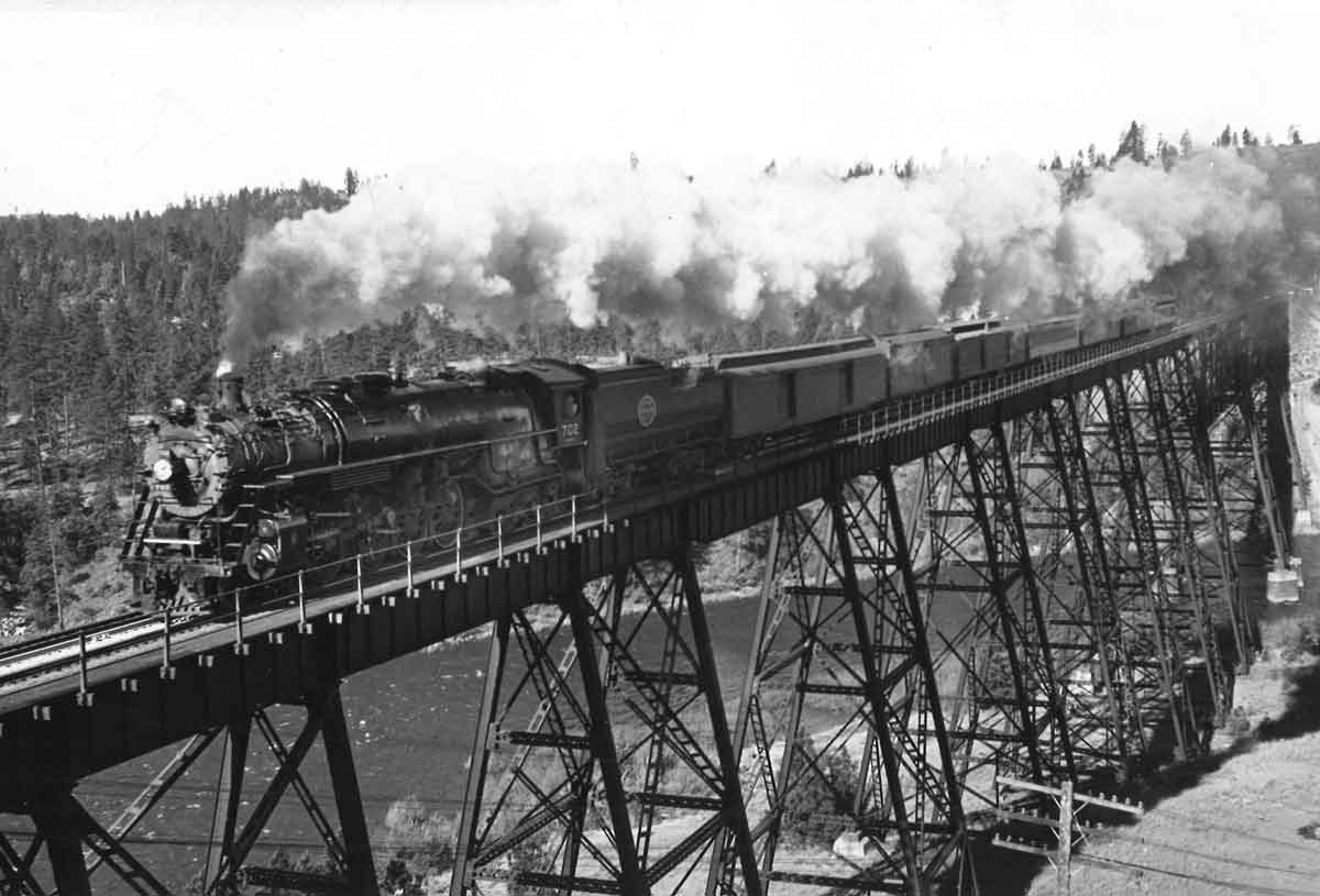 A steam engine and train on a tall wooden bridge