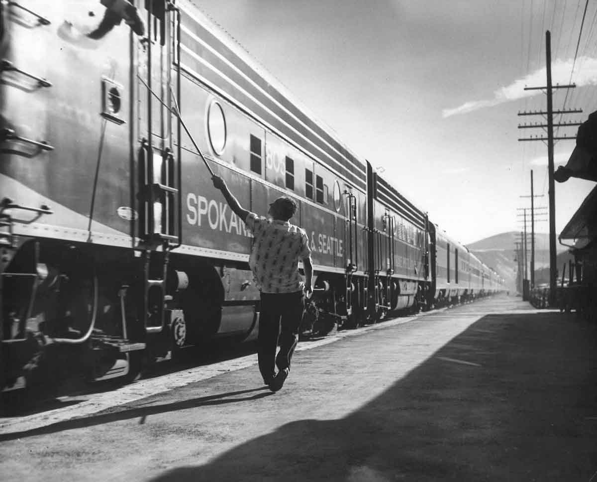 A black and white photo of a person walking by passenger cars