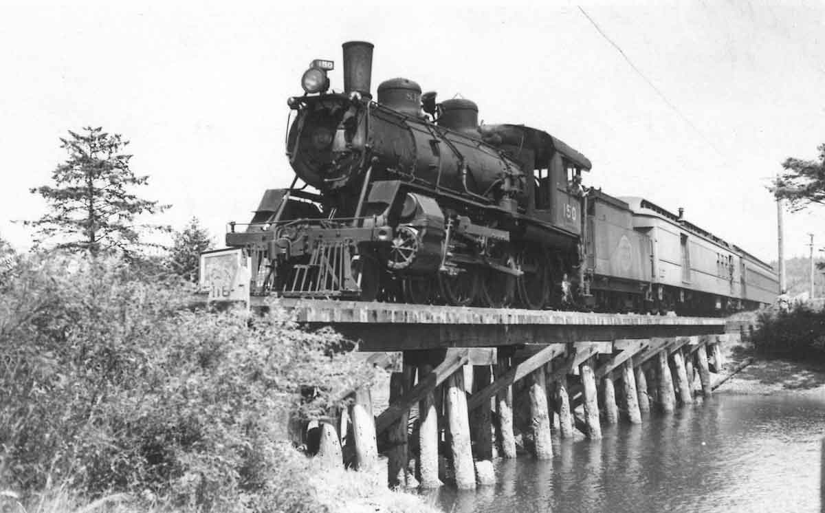 A black and white photo of a steam engine on a wooden bridge