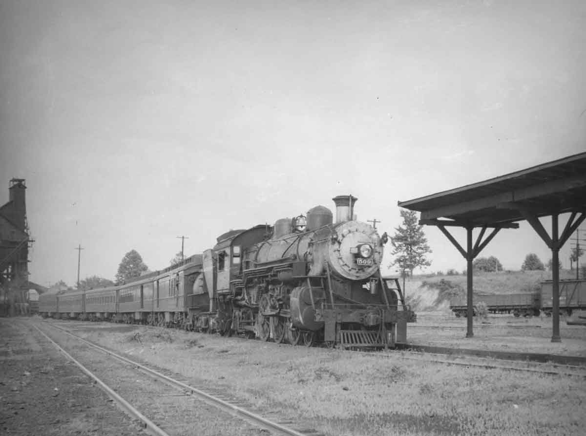 A black and white photo of a train parked outside a station