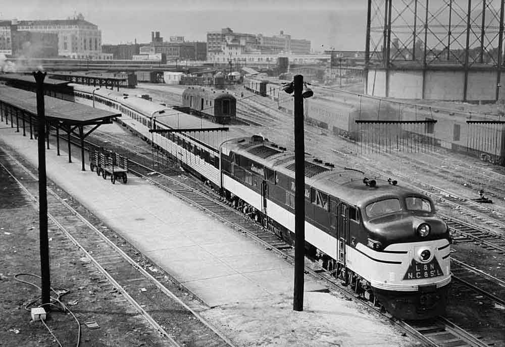 A black and white photo of a train parked outside a station