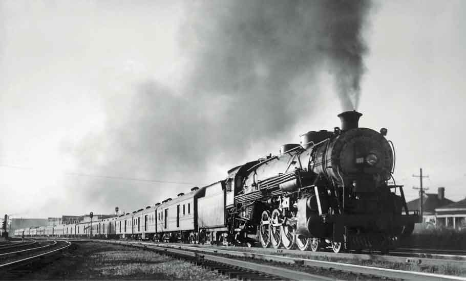 A black and white photo of a train approaching a station